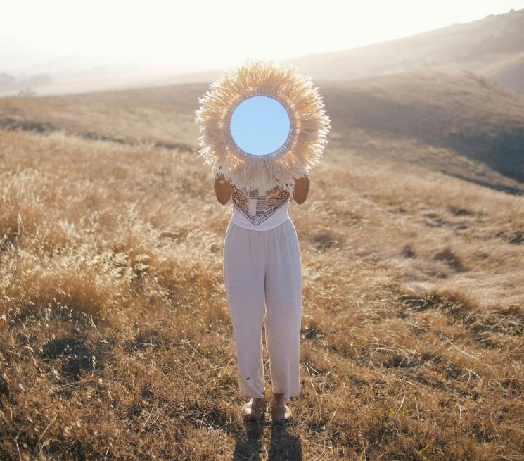 Kobieta na tle wzgórz trzyma lustro zakrywając twarz
