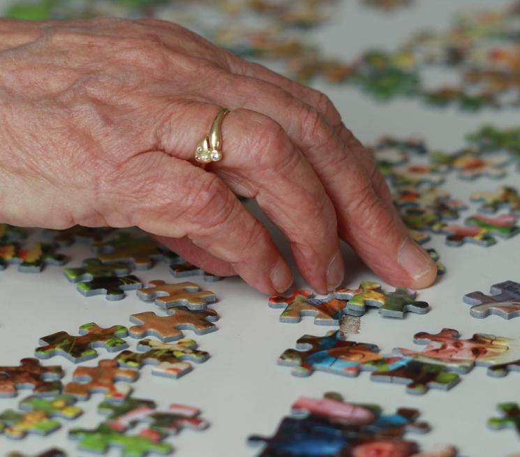 zdjęcie dłoni starszej kobiety układającej puzzle