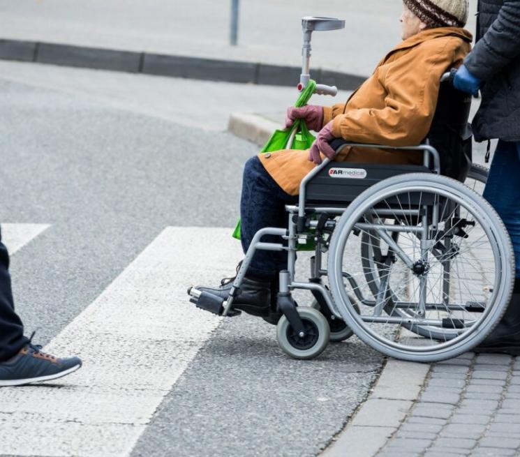osoba na wózku inwalidzkim z asystentem przechodzą przez przejście dla pieszych