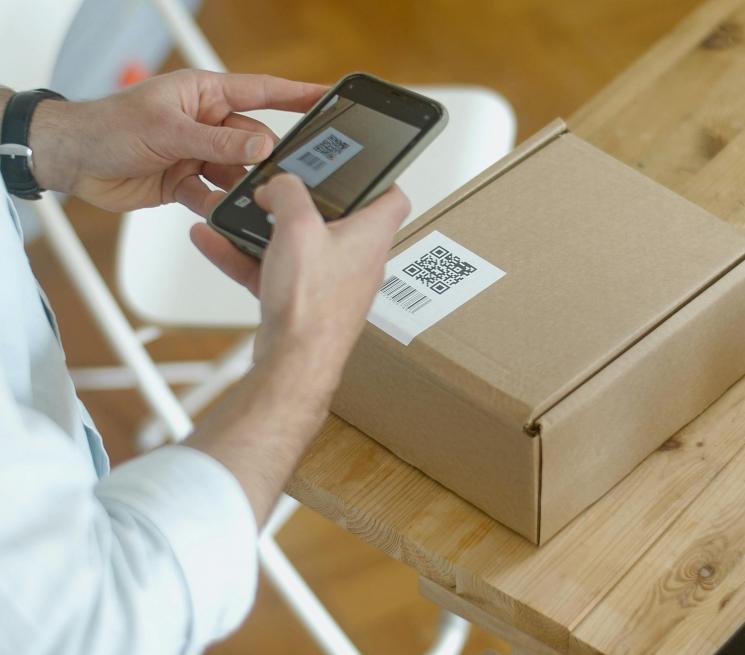 zdjęcie ręce osoby trzymającej smartfon i skanującej etykietę na paczce