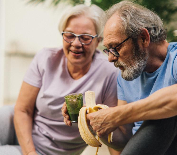zdjęcie para seniorów siedzi na matach pije sok i je banana