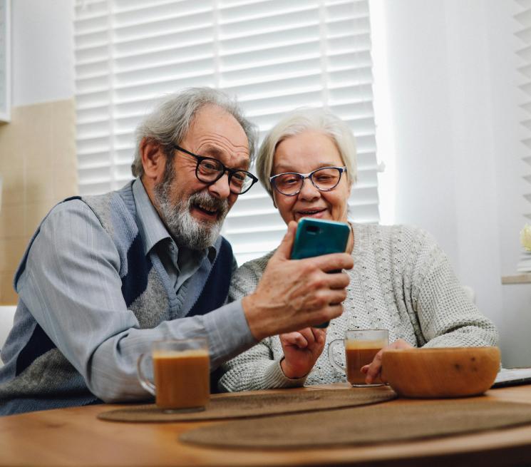 zdjęcie para seniorów siedzących przy stole patrzy w telefon