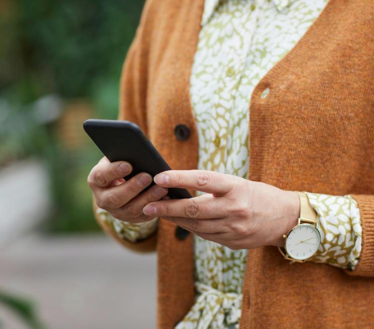 zdjęcie klatki piersiowej kobiety ubranej w sukienkę we wzory i brązowy sweter trzymającej telefon