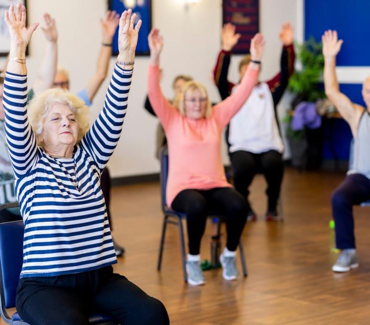 zdjęcie seniorzy siedzą na krzesłach i się gimnastykują