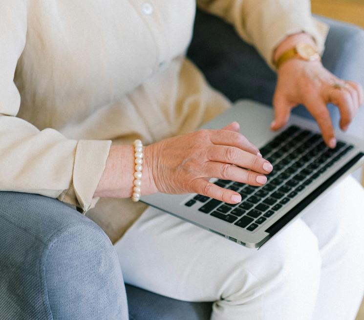 zdjęcie starsza kobieta w jasnych ubeaniach siedzi na fotelu i pracuje na laptopie