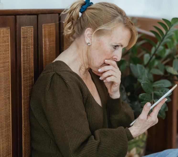 zdjęcie starsza kobieta patrzy zmatwiona na telefon trzymany w dłoni