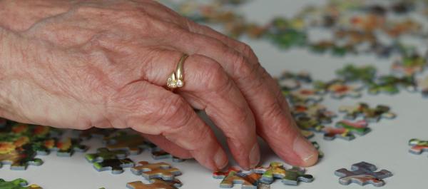 zdjęcie dłoni starszej kobiety układającej puzzle