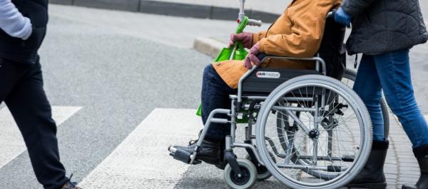 osoba na wózku inwalidzkim z asystentem przechodzą przez przejście dla pieszych