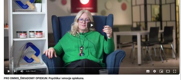 zdjecię kadr z filmy kobieta w zielonym sfetrze siedzi na fotelu i opowiada