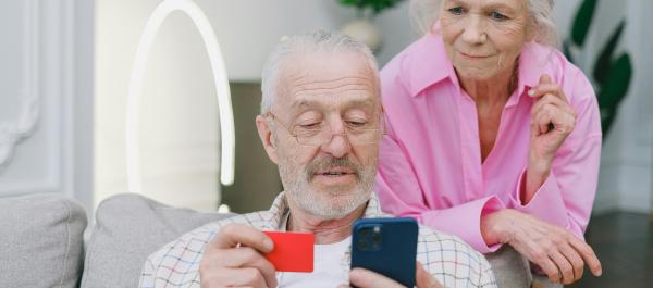 zdjęcie para seniorów mężczyna siedzi na kanapie trzyma telefon i kartę płatniczą