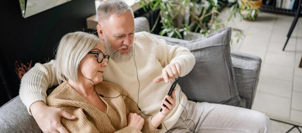 para seniorów siedzi na kanapie i słucha muzyki przez słuchawki na telefonie