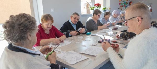 zdjęcie grupy seniorów siedzących przy stole i wykonujących prace plastyczne
