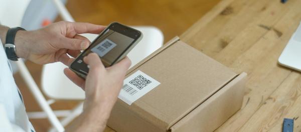 zdjęcie ręce osoby trzymającej smartfon i skanującej etykietę na paczce
