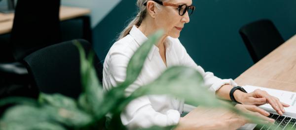 zdjęcie seniorka seidzi przy stole i pracuje na laptopie