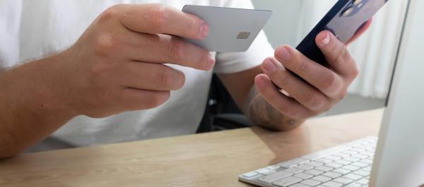 zdjęcie dłonie trzymające kartę bakomatową i telefon na biurku leży laptop