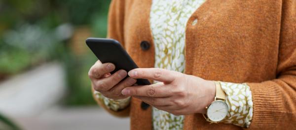zdjęcie klatki piersiowej kobiety ubranej w sukienkę we wzory i brązowy sweter trzymającej telefon