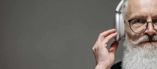 zdjęcie starszy mężczyzna w okularach z białą brodą ma złożone słuchawki i słucha muzyki