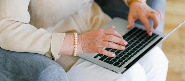 zdjęcie starsza kobieta w jasnych ubeaniach siedzi na fotelu i pracuje na laptopie