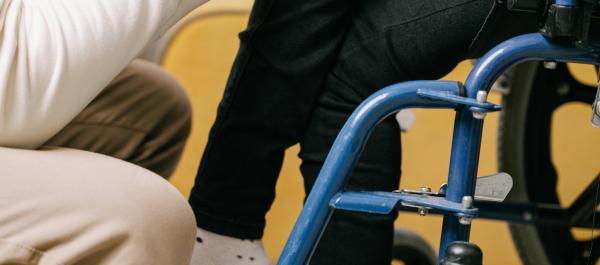 zdjęcie dwie osoby jedna siedządza na wózku inwalidzkim i kucający przy niej mężczyzna trzymają się za ręce