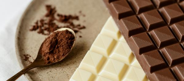 zdjęcie na talerzu leżą dwie tabliczki czekolady mlecznej i białej oraz łyżeczka z kakao