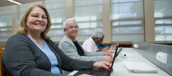 zdjęcie uśmiechnięci seniorzy kobieta i mężczyzna wykonują zadania na laptopach
