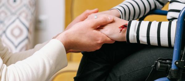 zdjęcie osoba kuca i trzyma za ręce kobietę siedzącą na wózku inwalidzkim