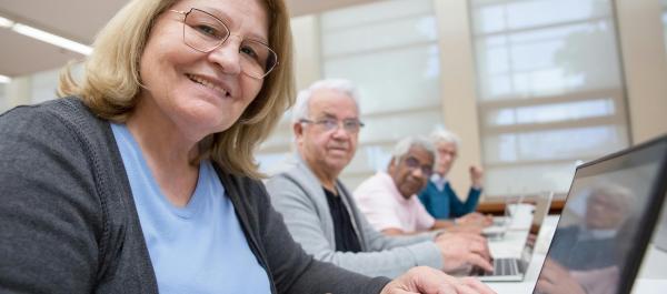 zdjęcie kilku seniorów siedzi przy biurkach i pracuje na laptopach uśmiechają się