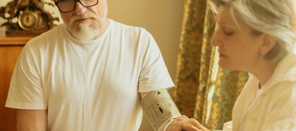 zdjęcie starsza kobieta i mężczyzna siedzą przy stole kobieta mierzy mężczyźnie ciśnienie za pomocą ciśnieniomierza