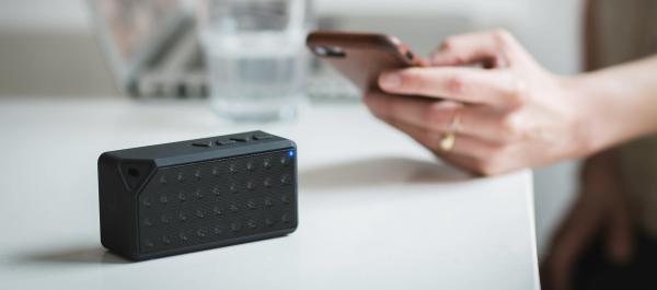 zdjęcie smartfon w dłoni obok leży mały czarny przenośny głośnik