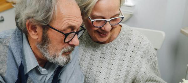 zdjęcie dwójka uśmiechniętych seniorów kobieta i mężczyzna pracują na laptopie