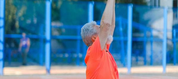 zdjęcie starszy mężczyzna w sporotywm ubraniu gimnastykuje sie na boisku