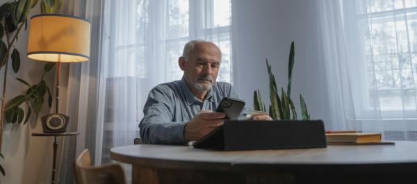 zdjęcie starszy mężczyzna siedzący przy stole patrzy w telefon