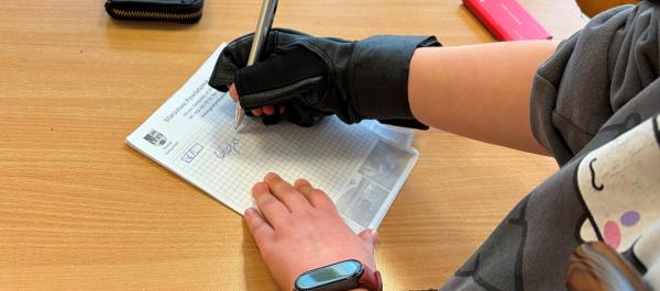 zdjęcie dziecko ma założoną rękwicę symylującą drżenie rąk i podpisuje się na kartce