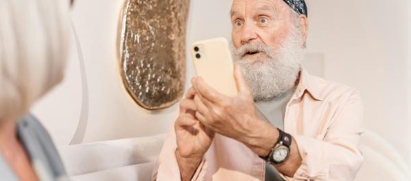 zdjęcie starszy mężczyzna z siwą brodą i chustą na głowie robi zdjęcie smartfonem siedzącej obok starszej kobiecie