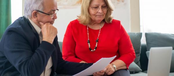 zdjęcie dwójka seniorów kobieta i mężczyzna siedzą przy stoliku z otwartym laptopem i przeglądają dokumenty