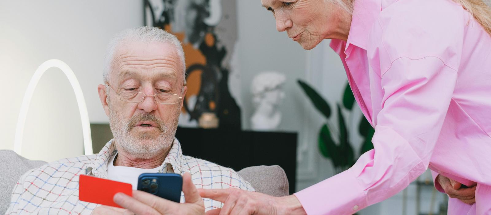 zdjęcie starszy mężczyzna trzyma telefon i kartę, a starsza kobieta pokazuju mu coś na telefonie