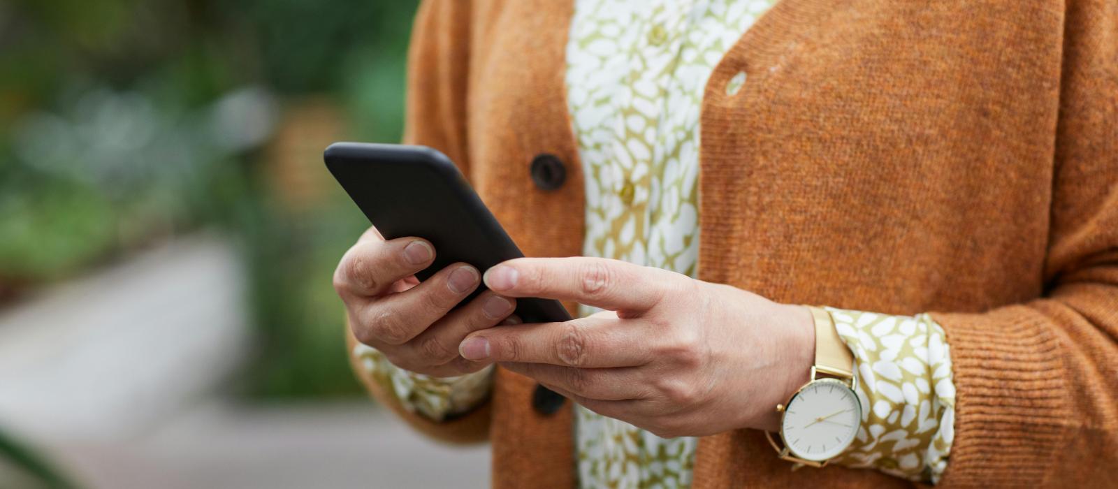 zdjęcie klatki piersiowej kobiety ubranej w sukienkę we wzory i brązowy sweter trzymającej telefon