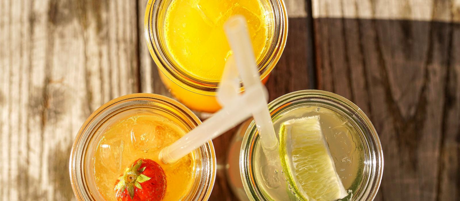zdjęcie z góry trzy szklanki wypełnione napojami lemoniadami z cytryną truskawą i pomarańczą