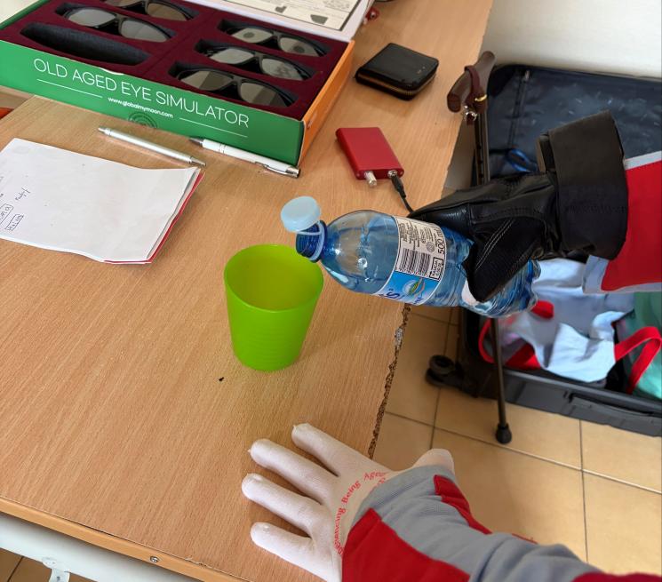 zdjęcie osoba w kombinezonie geriatrycznym nalewa wodę z butelki do kubka