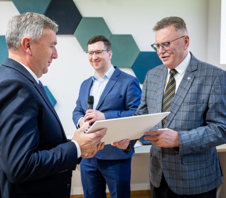 zdjęcie mężczyzna w garniturze wręcza drugiemu mężczyńnie w garniturze umowę grantową
