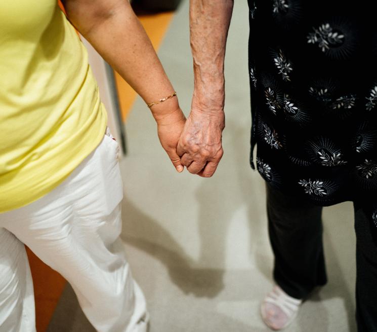 zdjęcie opiekunka trzyma starszą osobę za rękę idą razem