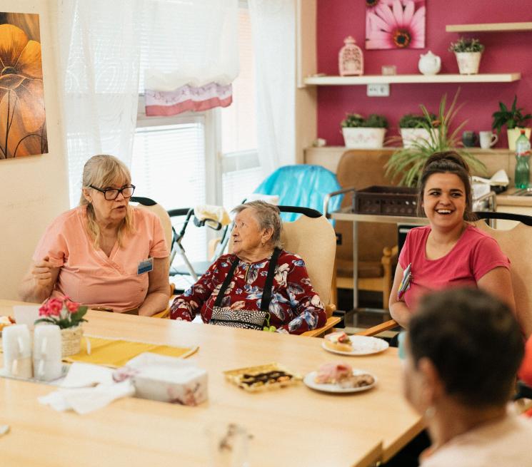 zdjęcie grupa seniorów siedzi przy stole wraz z opiekunami uśmiechają się przerwa kawowa