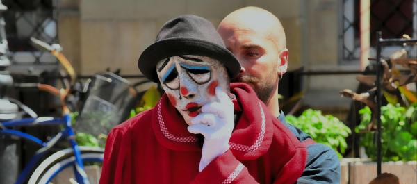 zdjęcie teatr uliczny mężczyna w czerwonym płaszczu w lewej dłoni w rękawiczce trzyma maskę w kapeluszu